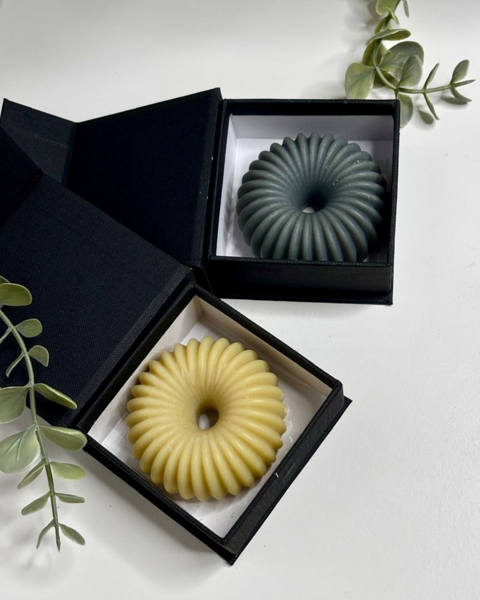 Coffret cadeau contenant deux galets de savon artisanaux aux formes striées (vert et jaune) dans des écrins noirs élégants.