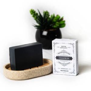 Savon au charbon noir sur son porte-savon en pierre avec sa boîte d'emballage blanche.