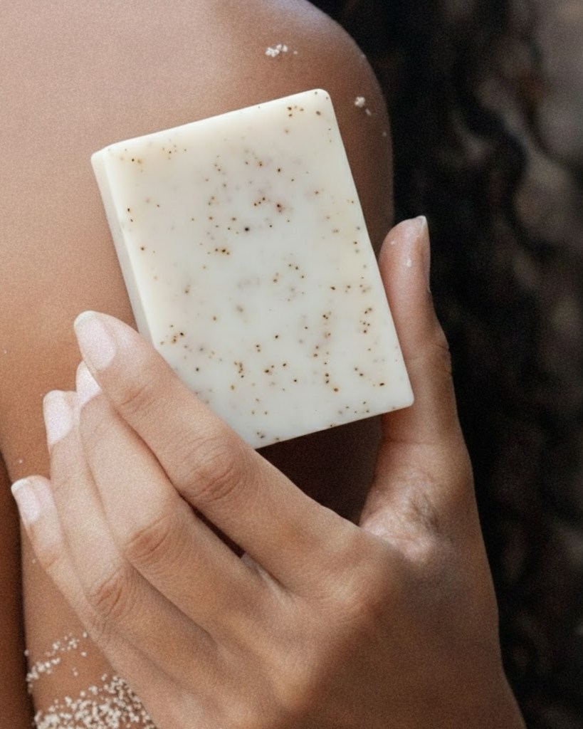 Main d'une personne tenant un savon exfoliant contre son épaule pour montrer l'application du produit.