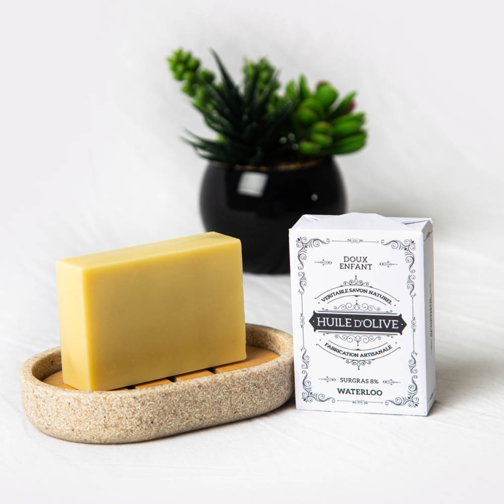 Savon à l'huile d'olive sur son support en pierre beige avec sa boîte d'emballage élégante.