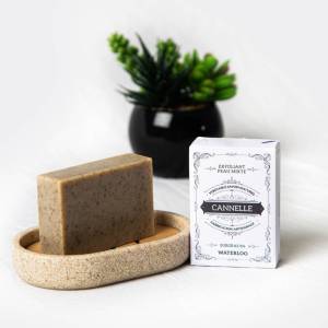 Savon à la cannelle sur son support avec son étui "Cannelle" et une plante décorative.