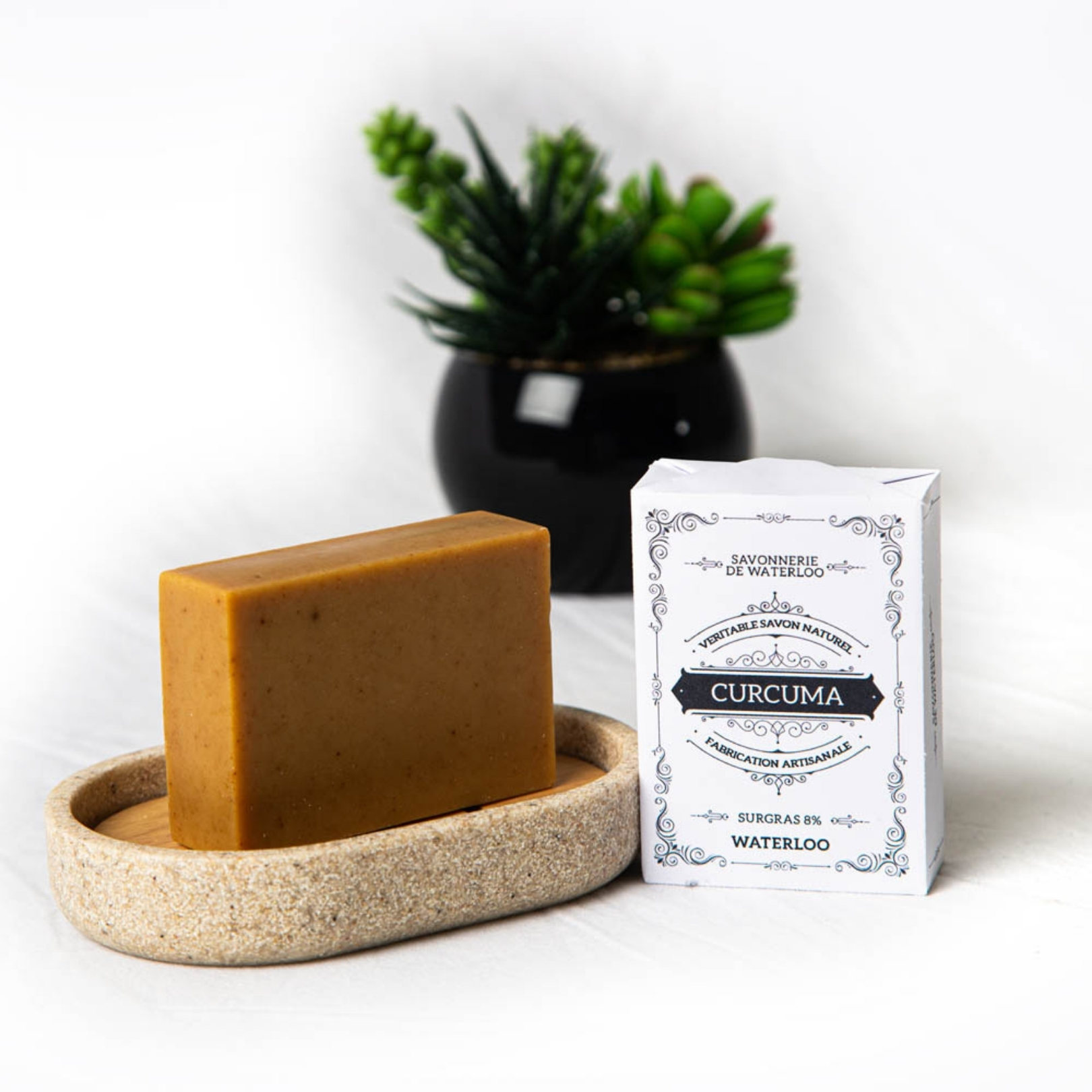 Savon au curcuma sur son porte-savon avec son emballage "Curcuma" et une petite plante verte.